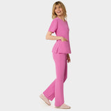 Bluza medyczna Emily w kolorze Disco Pink od Vena Uniformy.
Modelka stoi na jasnym tle w komplecie medycznym: bluza z krótkim rękawem oraz spodnie flare, zestawione z beżowymi sneakersami.