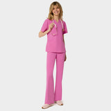 Bluza medyczna Emily w kolorze Disco Pink od Vena Uniformy.
Modelka stoi na jasnym tle w komplecie medycznym: bluza z krótkim rękawem oraz spodnie flare, zestawione z beżowymi sneakersami.