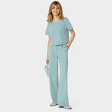 Bluza medyczna Gaja crop w kolorze CLOUDY BLUE od Vena Uniformy.
Modelka stoi na jasnym tle w pastelowym komplecie medycznym: bluza z krótkim rękawem oraz szerokie spodnie, zestawione z niebieskimi sneakersami.