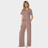 Bluza medyczna Gaja crop w kolorze LIGHT BROWN od Vena Uniformy.
Modelka stoi na jasnym tle w  komplecie medycznym: bluza z krótkim rękawem oraz szerokie spodnie, zestawione z beżowymi sneakersami.