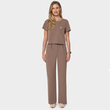 Bluza medyczna Gaja crop w kolorze MOCHA od Vena Uniformy.
Modelka stoi na jasnym tle w  komplecie medycznym: bluza z krótkim rękawem oraz szerokie spodnie, zestawione z beżowymi sneakersami.