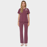 Bluza medyczna Emily w kolorze Dusty Plum od Vena Uniformy.
Modelka stoi na jasnym tle w komplecie medycznym: bluza z krótkim rękawem oraz spodnie flare, zestawione z beżowymi sneakersami.
